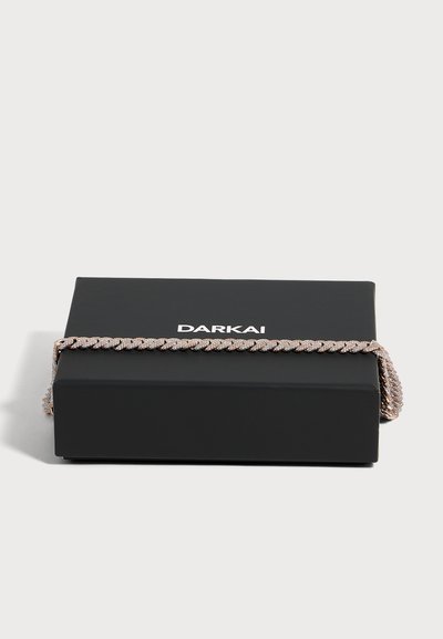 Bracelet chaîne cubain épaisse en or rose, recouvert de petits cristaux, reposant sur une boîte noire avec le logo DARKAI.
