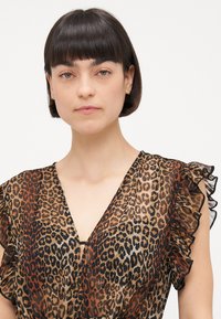 Vestido de cuello en V con estampado animal y mangas con volantes; presenta una mezcla de marrones, beige y negro en una tela ligera y transparente.
