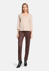 Beige geribbelde gebreide trui met V-hals, gecombineerd met bruine slim-fit broek van imitatiesuède en zwarte puntige enkellaarzen.