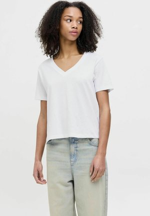 Camiseta de algodón blanca con mangas cortas y escote en V. Ajuste casual, textura suave, combinada con jeans de mezclilla de color azul claro.