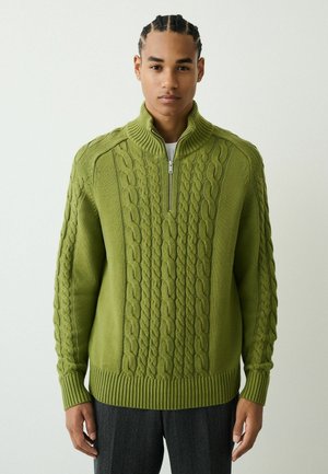 Grüner gestrickter Pullover mit hohem Kragen und Zopfmuster. Vorn mit Reißverschluss, gerippte Bündchen und Saum. Weiche Textur.