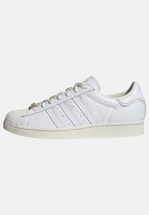 White low-top sneaker with shell toe, stitched stripes on the side, and white laces on an off-white sole.