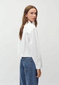 Camicia bianca con colletto, dal taglio relaxed e maniche lunghe, abbinata a jeans blu a vita alta. Tessuto morbido, design minimalista.