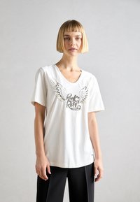 Vit bomullströja med V-ringning, korta ärmar, med broderade vingar och "Rock & Roll" i ett dekorativt typsnitt.