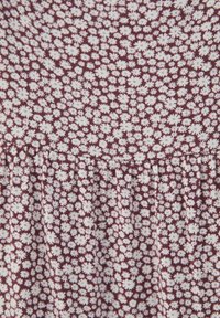 Tissu bordeaux avec un motif floral blanc, présentant un design froncé en bas créant texture et dimension.