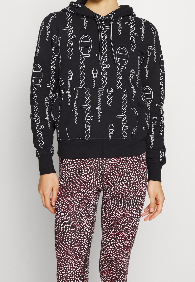 Haut à capuche noir avec impression du logo Champion en blanc, doté d'une poche avant et d'une capuche réglable. Accompagné de leggings colorés et à motifs.
