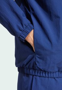 Mörkblå jacka med elastiska ärmslut och midja. Tillverkad av lättviktsmaterial, med en sidficka med en slät textur.