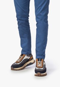 Sneakers da uomo caratterizzati da un mix di tessuto blu navy, rete grigia e suede marrone. Suola robusta con battistrada in gomma e lacci bianchi a contrasto.
