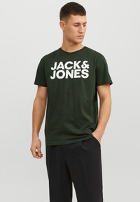 Camiseta de algodón en verde oliva con gran texto blanco "JACK & JONES" en el pecho, cuello redondo y mangas cortas.