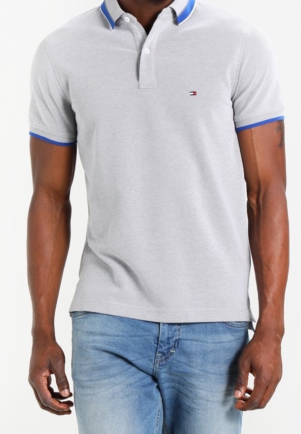 Polo gris avec empiècements bleu au col, manches courtes et un petit logo brodé. Porté avec un jean bleu clair. Tissu texturé.