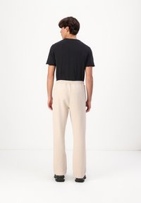 Schwarzes T-Shirt mit kurzen Ärmeln, kombiniert mit hellbeigen, lässig geschnittenen Hosen. Das Outfit zeichnet sich durch ein einfaches Design und einen weichen Stoff aus.