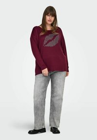 Bordeaux langermet skjorte med et sølvfarget leppekiss-grafikk, kombinert med lysegrå, rette jeans og svarte ankelstøvler.