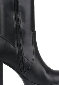 Botín negro de cuero hasta el tobillo con cremallera lateral, tacón cuadrado, textura suave y un diseño ajustado con detalles de costura geométrica.