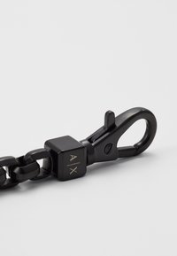 Chaîne en métal noir avec un fermoir carré portant les lettres gravées A/X. Le fermoir comprend un crochet à ressort pour un attache sécurisée.