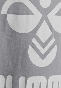Diseño gráfico blanco sobre tela gris, que presenta grandes formas circulares y triangulares con líneas texturizadas, creando un patrón audaz y moderno.