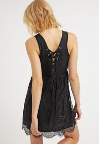 Black lace dress with a fitted bodice, V-back, and lace-up detail. Features a flared skirt and a delicate lace trim at the hem.