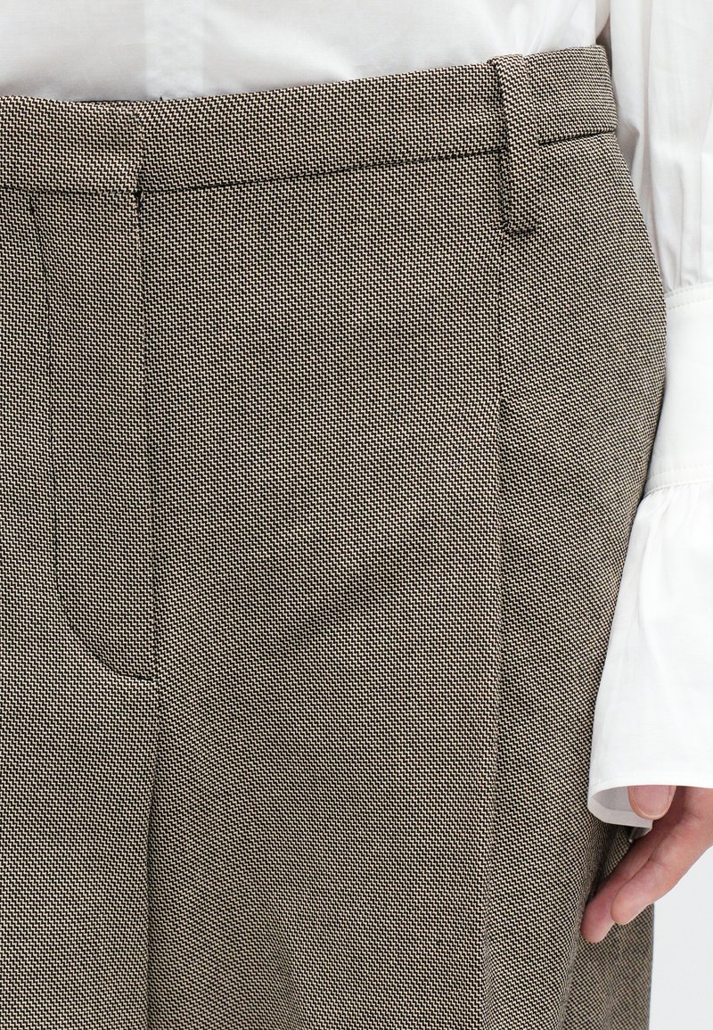 Pantaloni in un tessuto marrone texture con un sottile motivo a zigzag. Presentano tasche laterali e una silhouette slim con cuciture sartoriali.