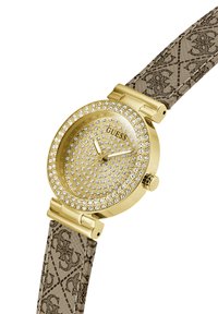 Reloj de pulsera en tono dorado con un bisel brillante, correa texturizada beige con un patrón de logo repetido y esfera con tachuelas.