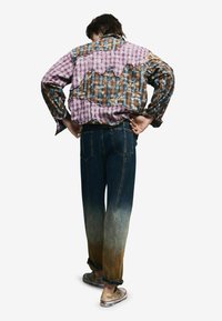 Foltos farmerdzseki kockás mintákkal, lila és barna textúrákkal; elhalványult, bő szabású kék farmerrel és kopott cipőkkel párosítva.