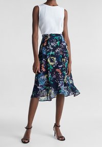 Blommig A-linjeformad kjol i marinblått, med färgglada blommönster, kompletterad med en vit ärmlös topp och svarta klacksandaler.