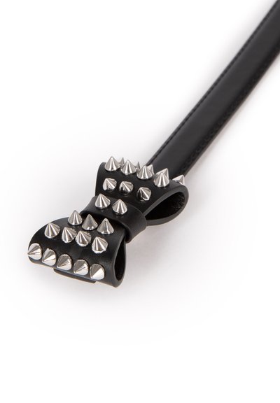 Zwarte leren boog met zilveren metalen spikes die zijn bevestigd aan een dunne zwarte leren riem op een witte achtergrond.