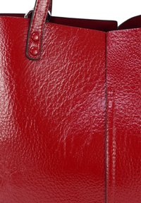 Glanzende rode leren handtas met een gestructureerd oppervlak, zichtbare handgreep bevestigd met twee rode knopen, en zwarte randafwerking.