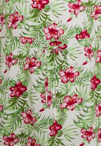 Tecido branco com um grande padrão floral apresentando flores de hibisco vermelhas e folhas de palmeira verdes, amarrado na cintura com um cinto de tecido à conjuntar.