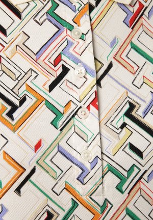 Chemise à bouton avec un motif géométrique multicolore sur fond clair, ornée de boutons ronds blancs et en tissu texturé.