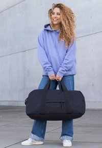 Schwarze Sporttasche mit stabilen Griffen, die über eine Vordertasche verfügt. Das Material wirkt strapazierfähig und die Textur ist glatt. Einfaches Design, keine auffälligen Muster.