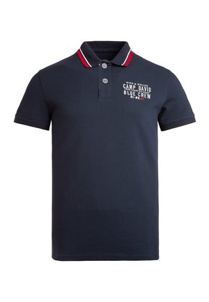 Polo shirt à manches courtes bleu marine avec col à rayures rouges et blanches et texte imprimé blanc sur la poitrine gauche.