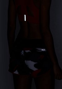 Baksidan av en person som bär en reflekterande sport-bh och shorts med kamouflagemönster i svagt ljus.