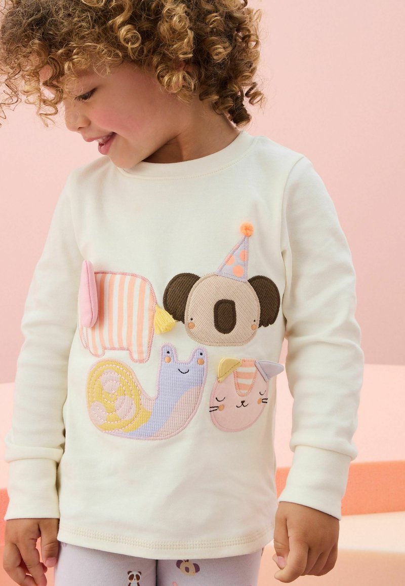 Krämfärgad långärmad skjorta med färgglada djurapplikationer: en koala, snigel och katt, med texturerade tyger och lekfulla mönster.