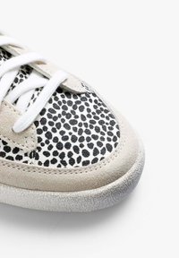 Sneaker z teksturowanym czarno-białym wzorem w kropki na zamszowej cholewce, jasne sznurowadła oraz gumowa podeszwa z drobnym wzorem zapewniającym przyczepność.