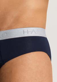 Slip navy blu con una leggera cintura elastica grigia con testo in rilievo, tessuto liscio e dettagli di cucitura a contrasto lungo i bordi.