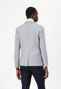 Helehall blazer, mis on valmistatud tekstureeritud kangast. Omab kohandatud lõiget, sisselõigatud krae ja ühte tagumist venti. Näha on ka tumehallad püksid.