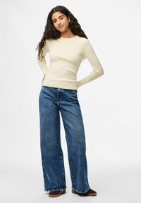 Crème ribbad långärmad topp i kombination med blå vida denimjeans. Jeansen har en klassisk femficksdesign och fransad fåll.