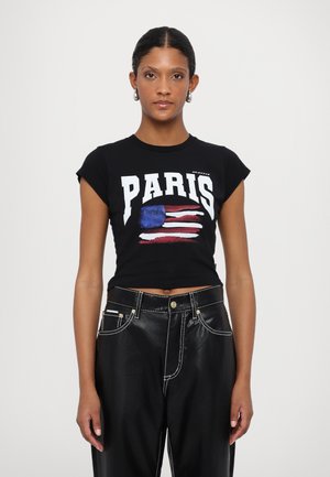 Black cropped T-shirt featuring "PARIS" in bold white text and a flag design. Paired with black leather pants with white stitching accents.