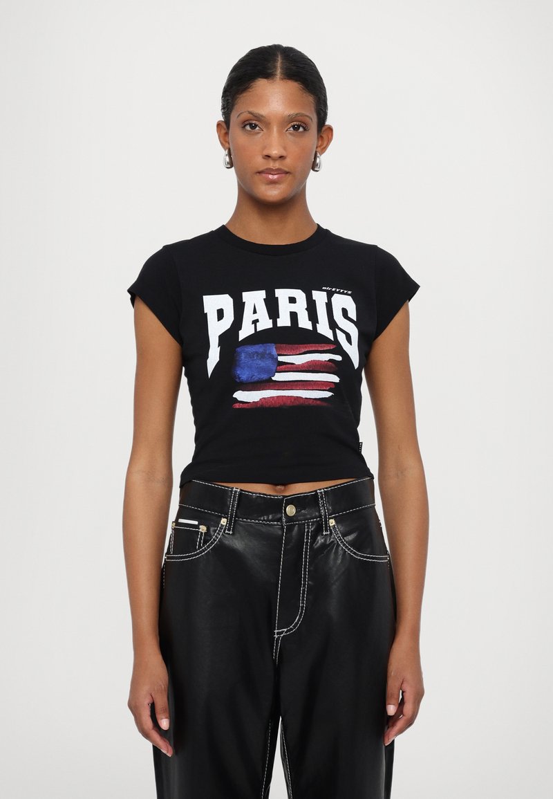 Black cropped T-shirt featuring "PARIS" in bold white text and a flag design. Paired with black leather pants with white stitching accents.