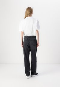 T-shirt blanc à manches courtes associé à un jean ample gris foncé. Le jean possède un design classique à cinq poches et des détails de couture subtils.
