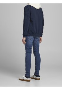 Marinblå bomberjacka med vit huva, strukturerat material, ribbade muddarna. Buren med blå jeans och vita sneakers med marinblå accenter.