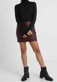 Schwarzer Rollkragenpullover, slim fit, lange Ärmel, kombiniert mit einem burgunderfarbenen Leder-Minirock. Schwarze Stiefeletten mit chunky Sohlen.