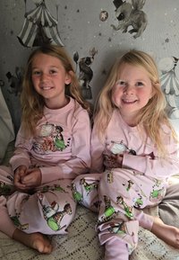 Light pink pajamas feature playful animal illustrations in green outfits. The fabric appears soft, with long sleeves and elastic cuffs.