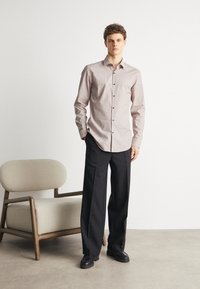 Camicia bianca e bordeaux a fantasia con maniche lunghe e bottoni neri, abbinata a pantaloni neri a gamba larga e scarpe nere.