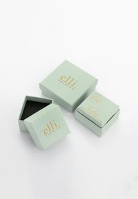Twee mintgroene kartonnen dozen met gouden letters, waarvan er één open is en een zwarte binnenkant onthult, met een gladde textuur en vierkante vorm.