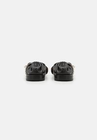 Zapatos de cuero negro con punta redonda y textura arrugada en el talón, con suela plana y diseño minimalista.