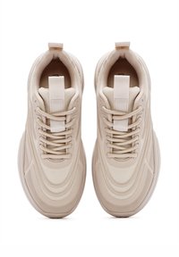 Beige Sneakers mit einem strukturierten Mesh-Obermaterial, auffälligen Nähten, flachen Schnürsenkeln und einer gepolsterten Zunge. Abrundete Gummisohle mit Profil.