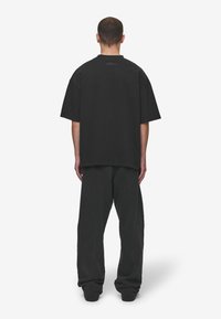 Black oversized t-shirt with short sleeves, round neckline, and a subtle logo detail on the back. Paired with loose-fitting black pants.