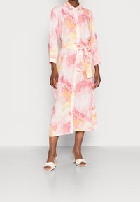 Langes, knöpfbares Hemdkleid mit einem pastellfarbenen Aquarellmuster in Rosa, Orange und Gelb. Mit einem Taillengürtel und umschlagbaren Ärmeln.
