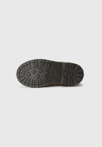 Semelle de chaussure en caoutchouc noir avec de profondes rainures et une surface texturée, comportant une étiquette rectangulaire et des motifs en relief pour la traction.