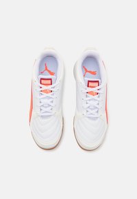 Baskets de sport blanches avec une texture lisse, ornées d'accents corail, de panneaux en mesh et d'une semelle en caoutchouc. Logo affiché de manière proéminente sur la languette.